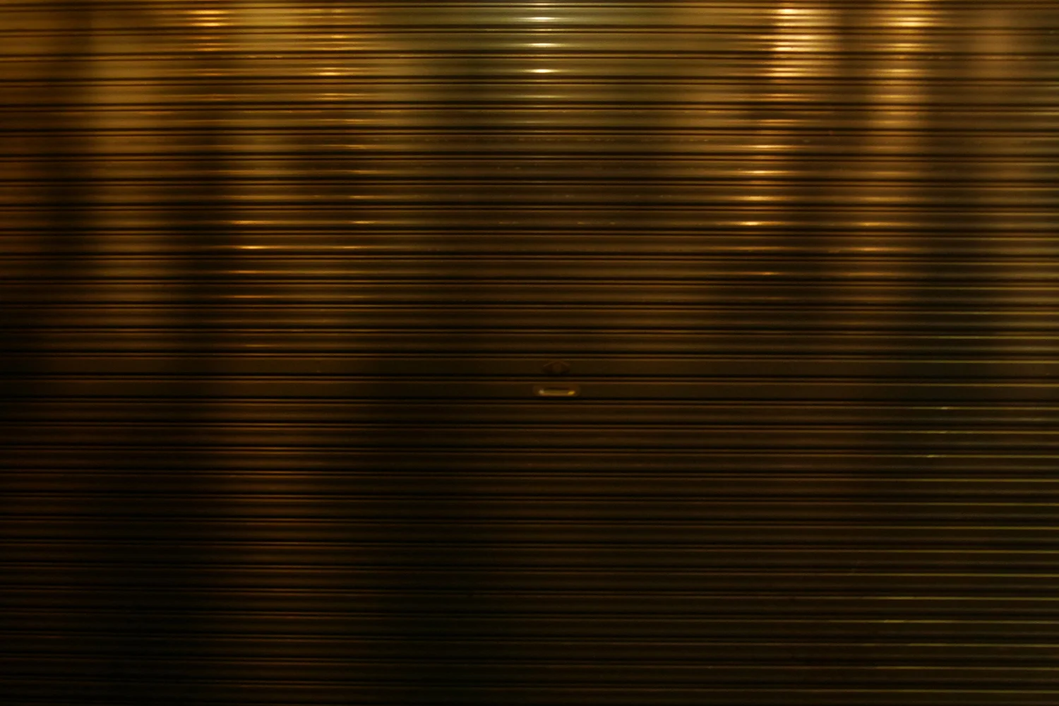 Analog photograph of a textured metal louvered shutter with warm golden light streaks, late-afternoon earthy glow